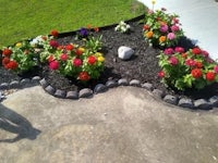 a flower bed in front of a house with rocks and flowers